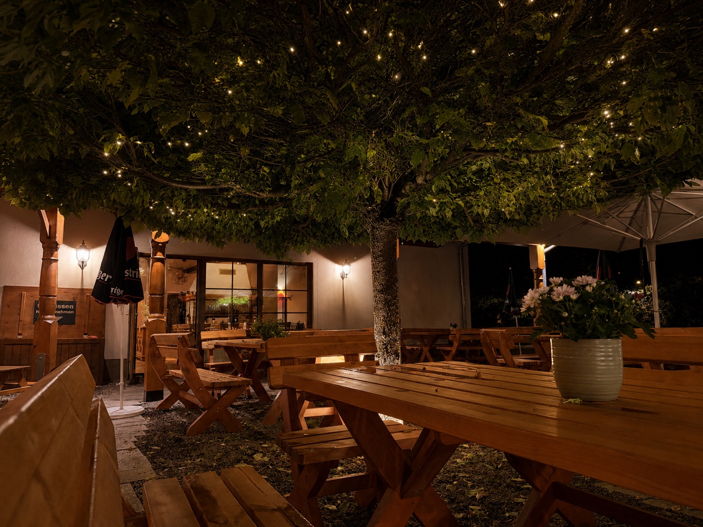 Großer Baum und gedeckte Holztische im Biergarten